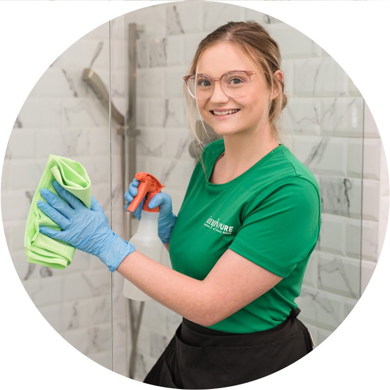 Cleaner wiping down glass shower door with eco-friendly cleaner