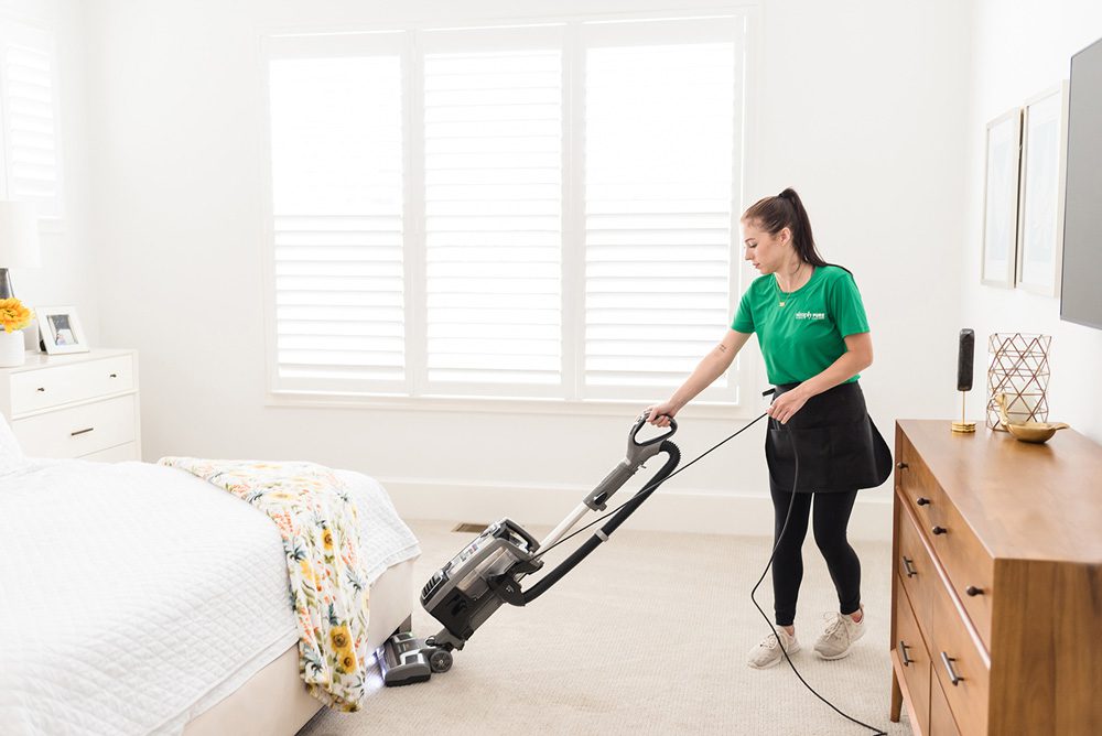 Professional cleaner vacuuming bedroom during Deluxe Deep Clean service